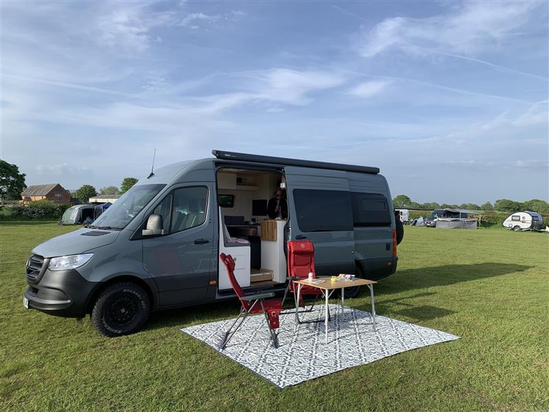 Van set up on campsite with outdoor chairs